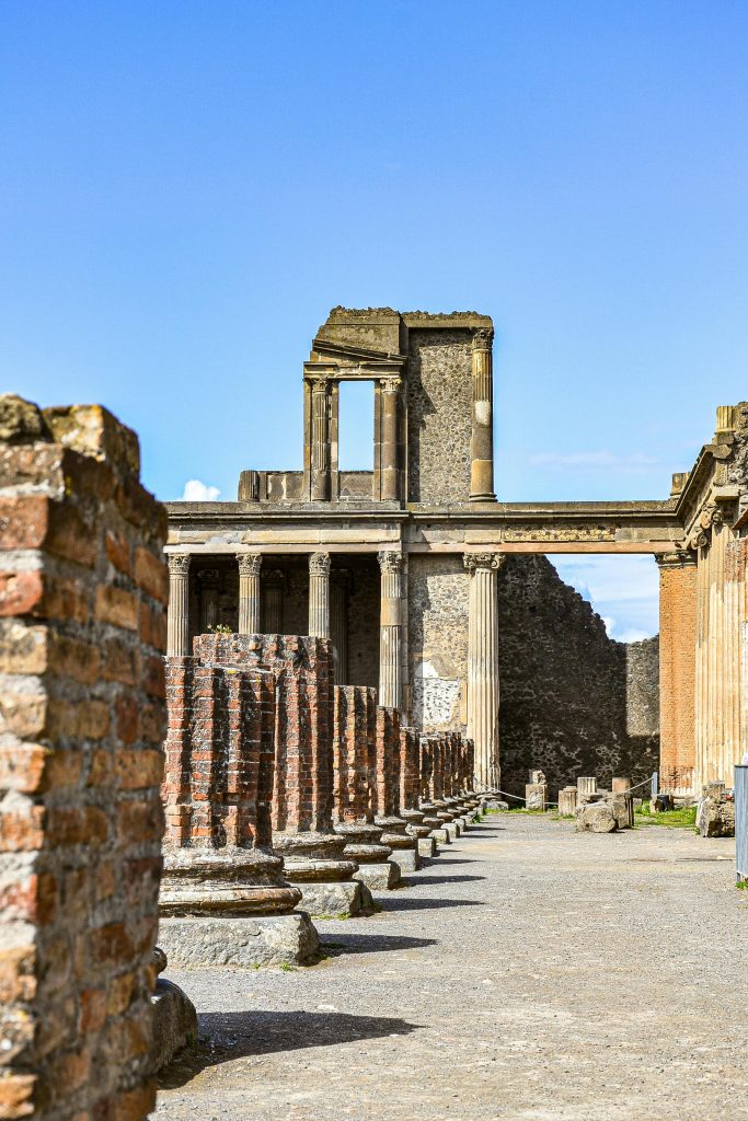 Explore the ancient ruins of Pompeii with iconic columns and buildings under a clear blue sky.
